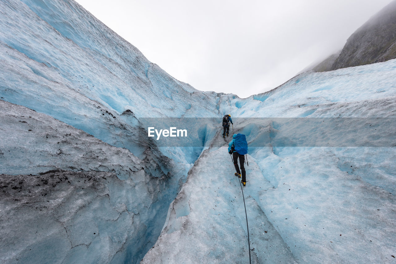 Rear view of hikers climbing glacier against sky
