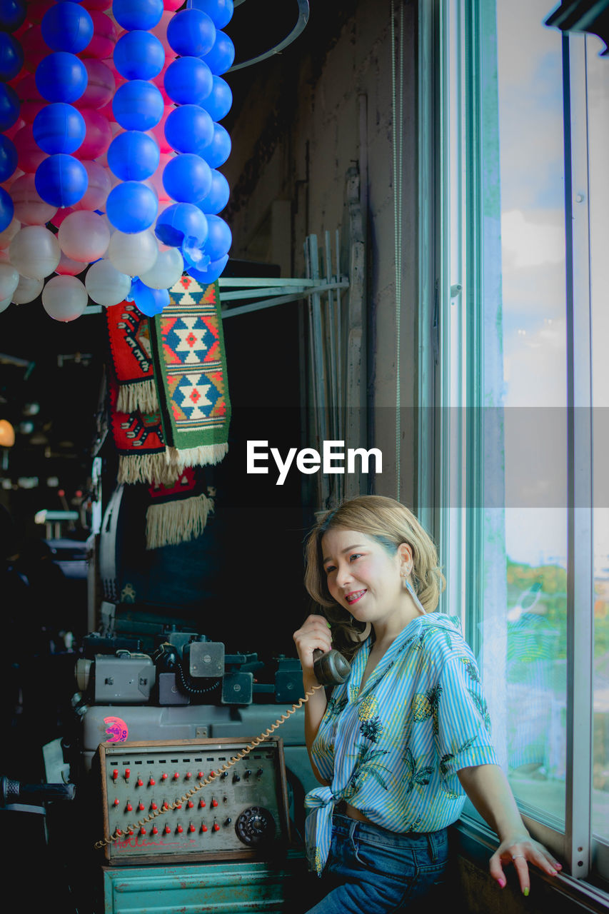 Smiling woman talking on phone while standing by window