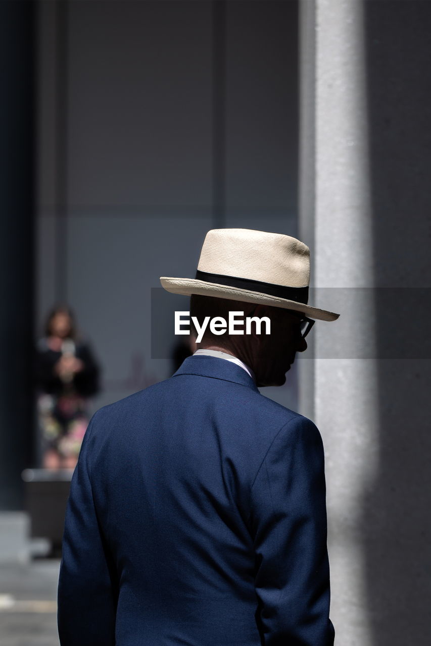 REAR VIEW OF MAN WEARING HAT AGAINST WALL