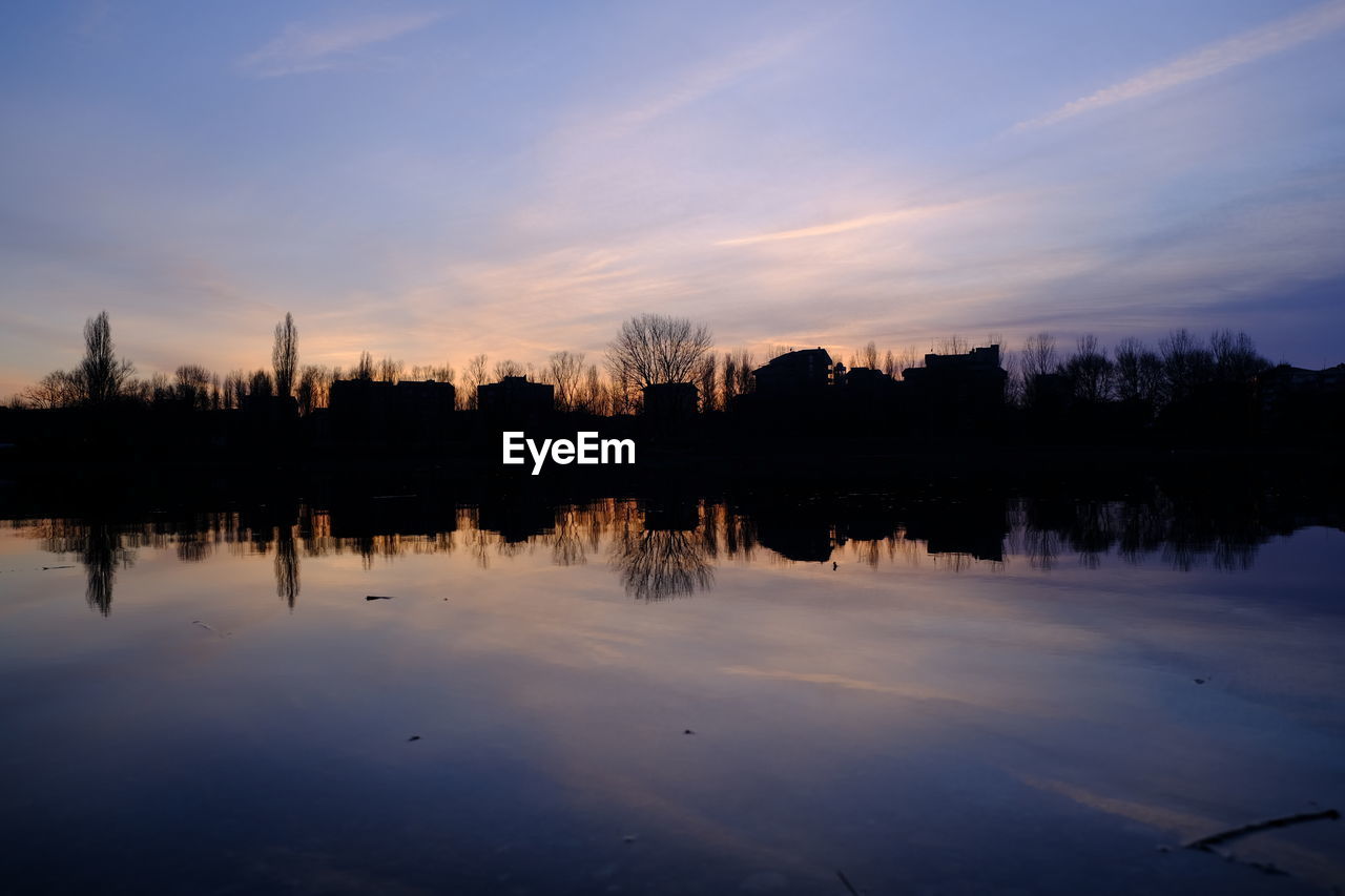 Silhouette trees by lake against sky during sunset