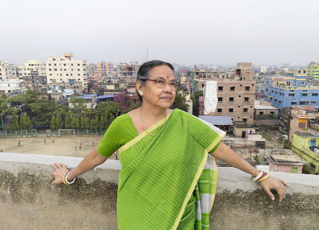 An aged bengali woman enjoying view of urban surroundings from rooftop of a building at howrah india