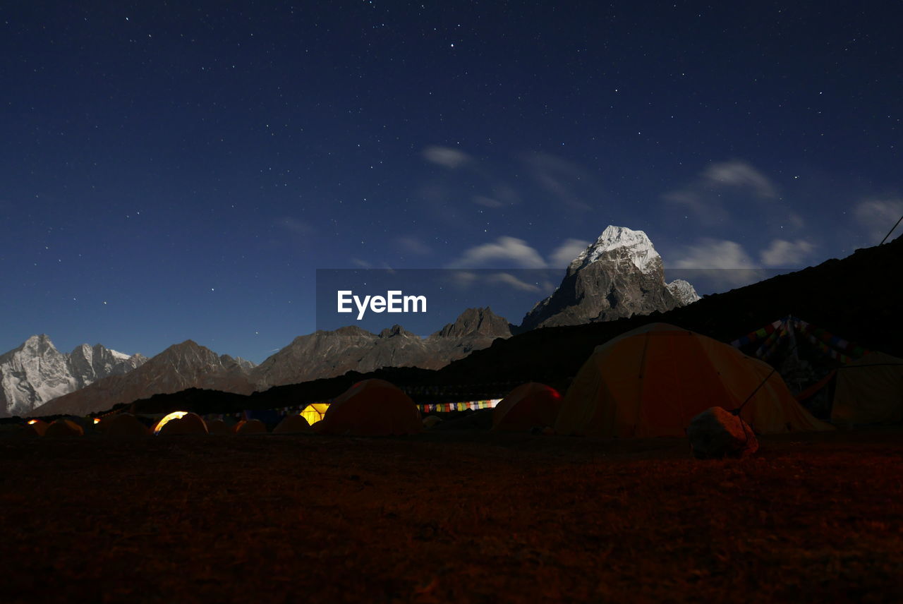 Tents by rocky mountains against sky at night