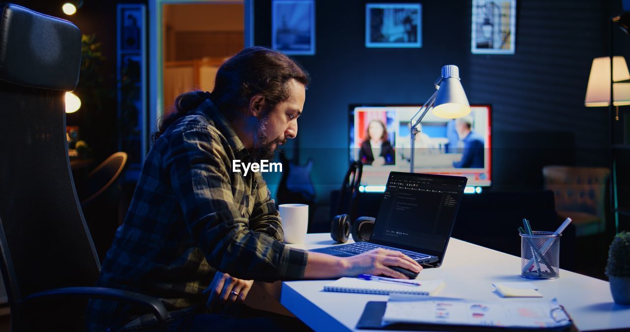 side view of man using laptop while sitting in cafe