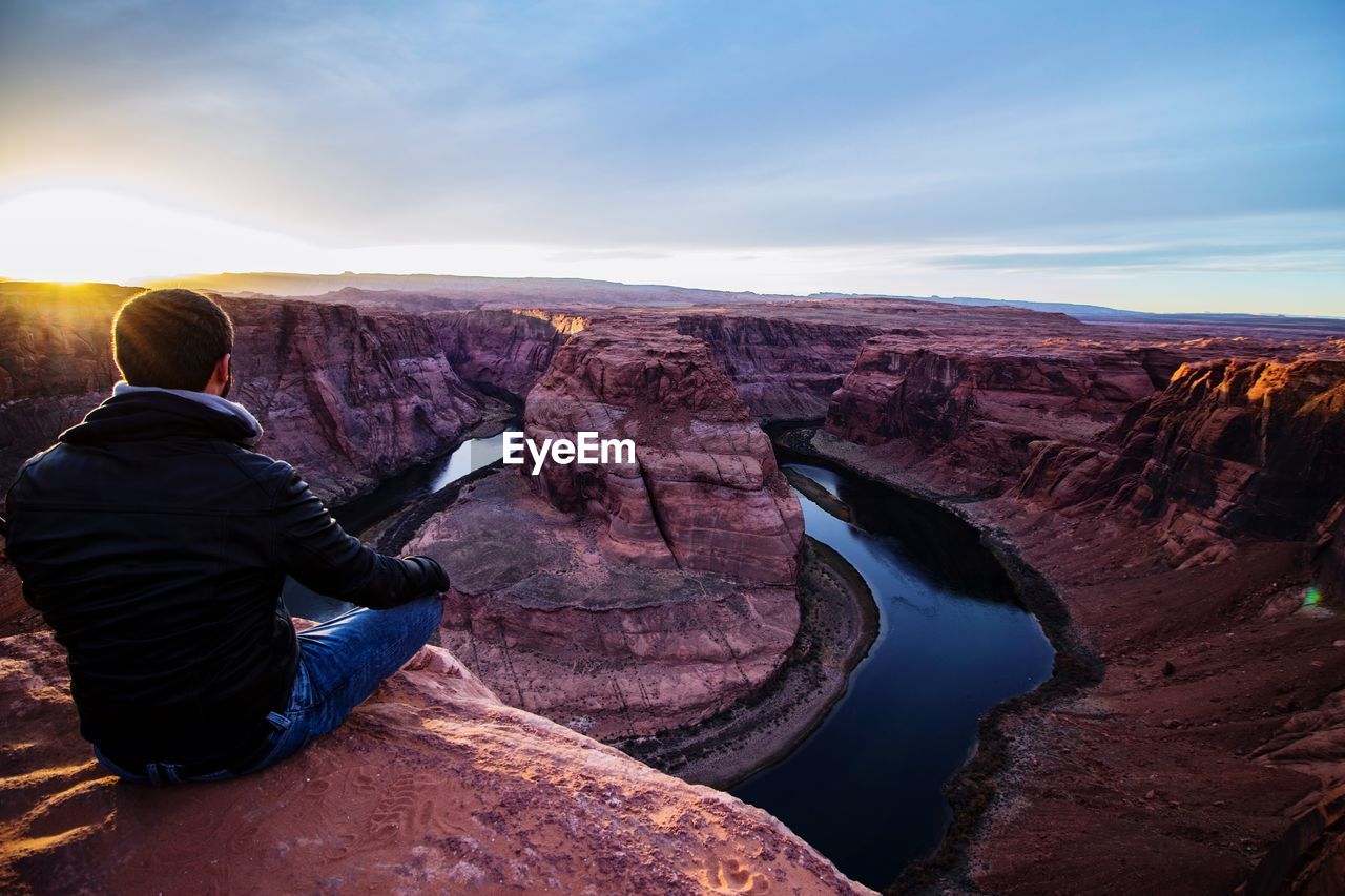 Rear view of man sitting at horseshoe bend against sky
