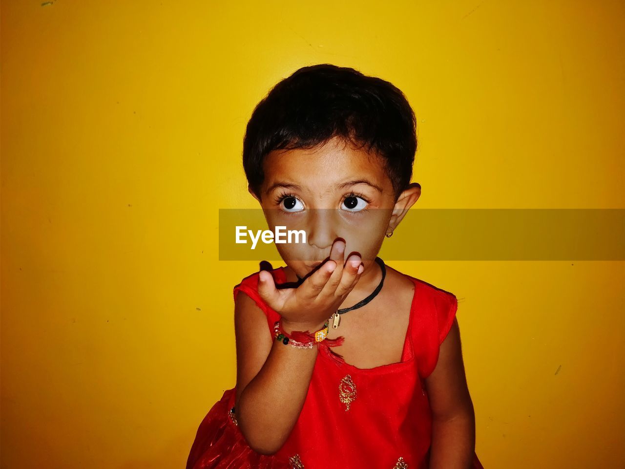 Girl covering mouth with hand against yellow background