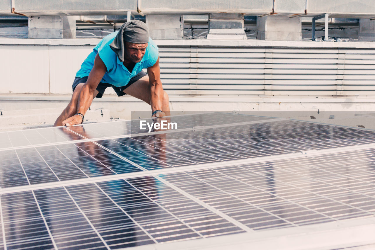 Serious male worker installing modern solar panels while working in industrial area of plant on sunny day