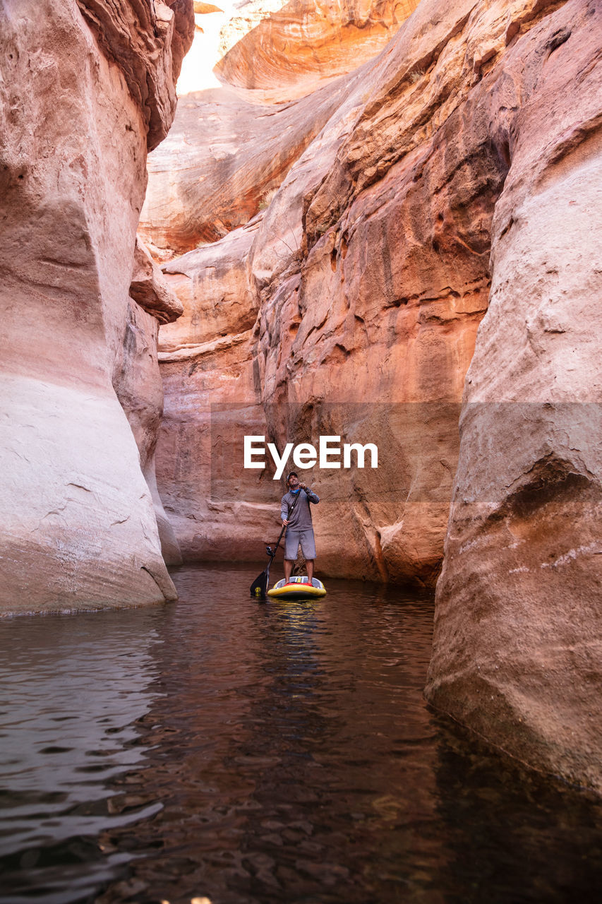 Man paddleboarding on lake amidst rock formations