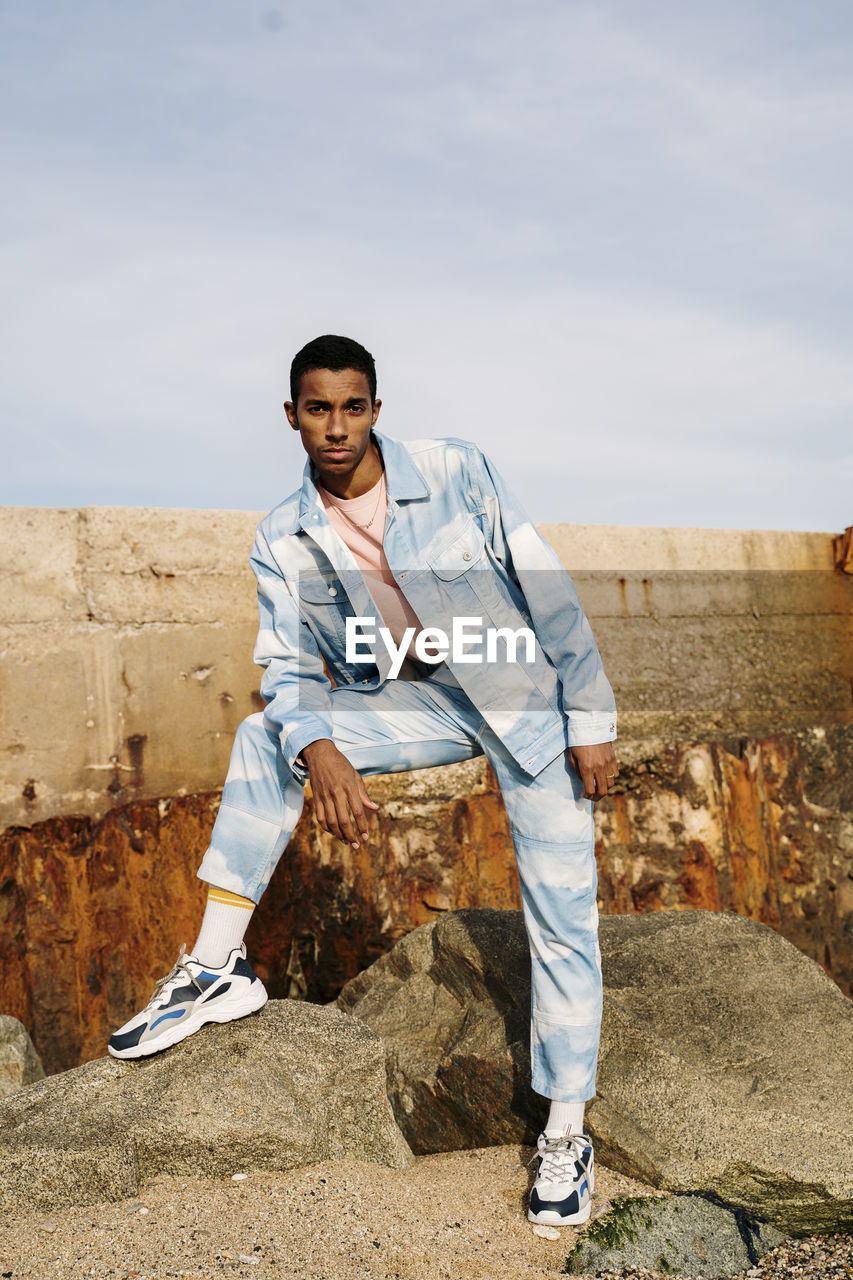 Man wearing clouds denim suit staring while standing on stone