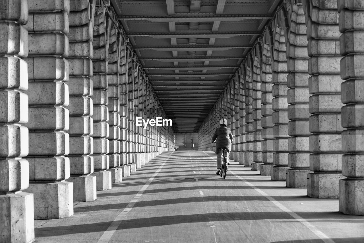 Rear view of person riding bicycle on road amidst colonnades