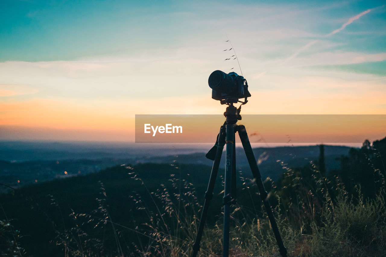 Silhouette camera on mountain against cloudy sky during sunset