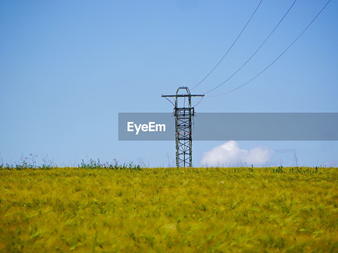 ELECTRICITY PYLONS ON FIELD AGAINST SKY