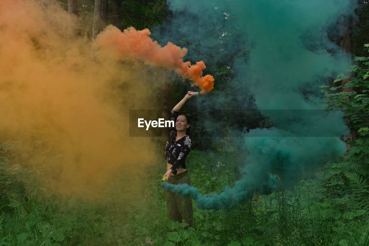 Woman standing by color smoke in forest