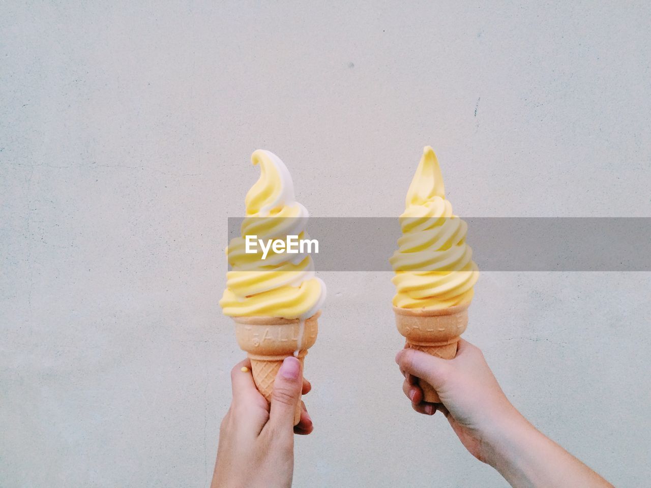 Woman holding ice cream cones against wall