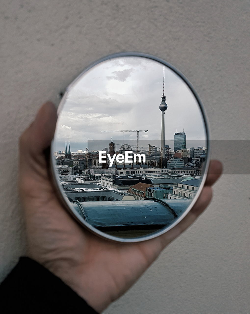 Cropped image on hand holding mirror with reflection of fernsehturm and cityscape