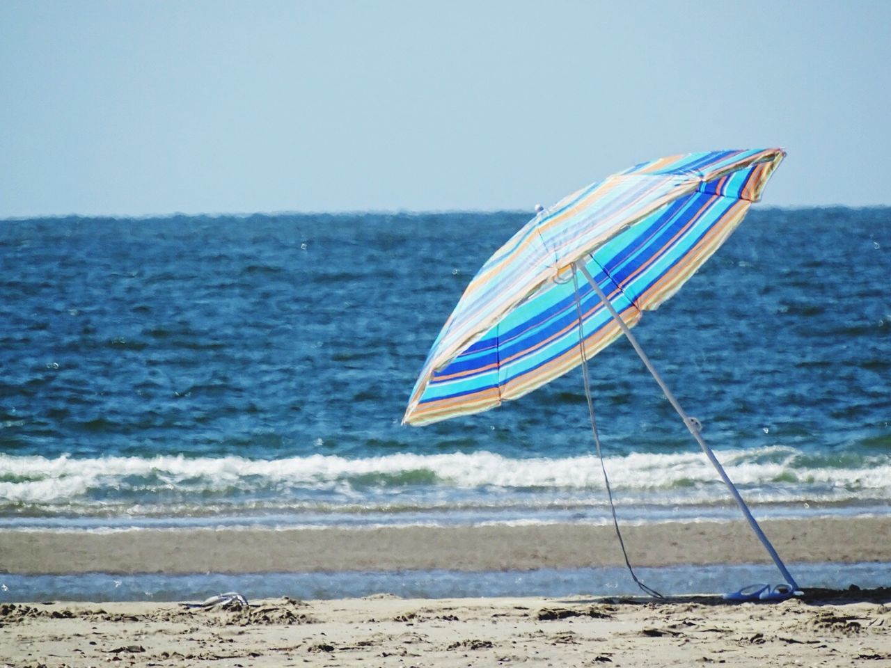 Beach umbrella on shore against clear blue sky