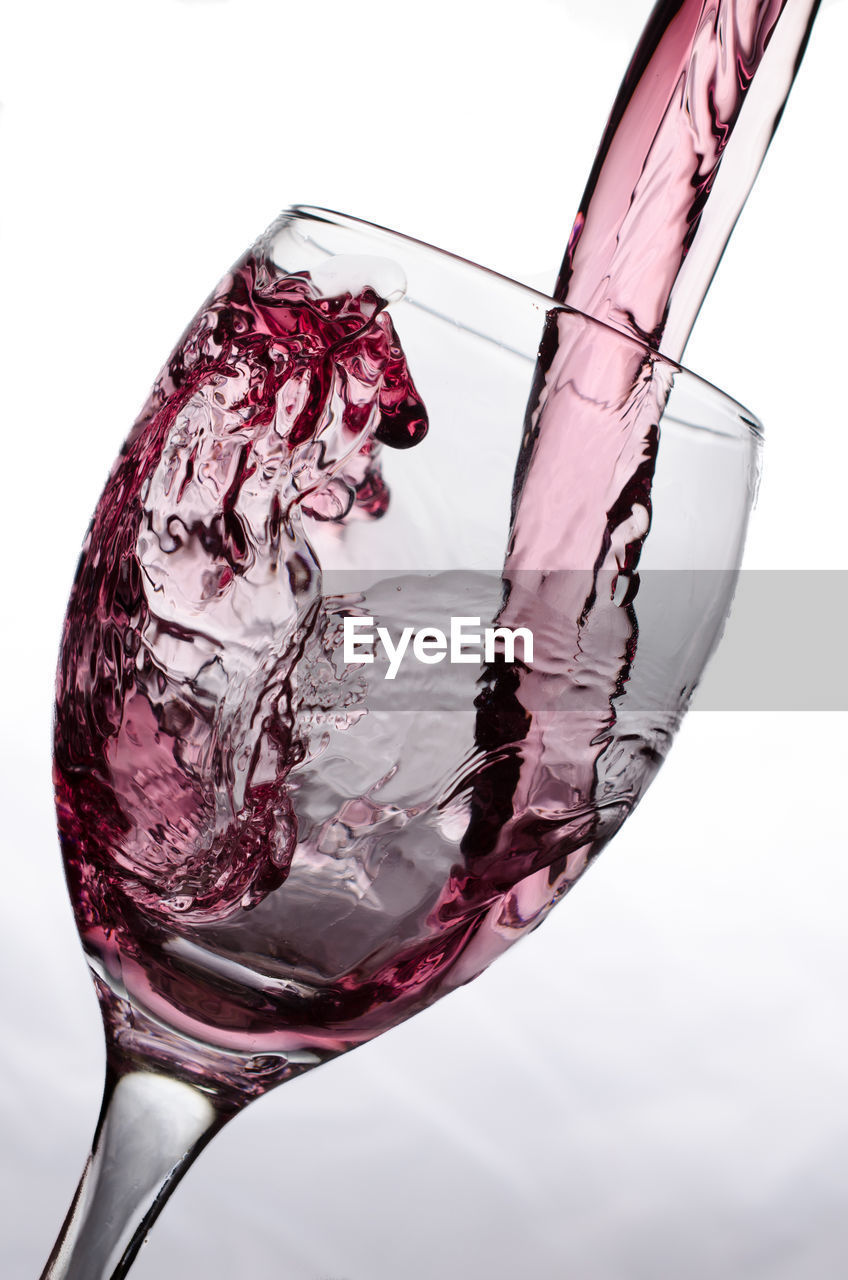Close-up of red wine pouring in glass against white background