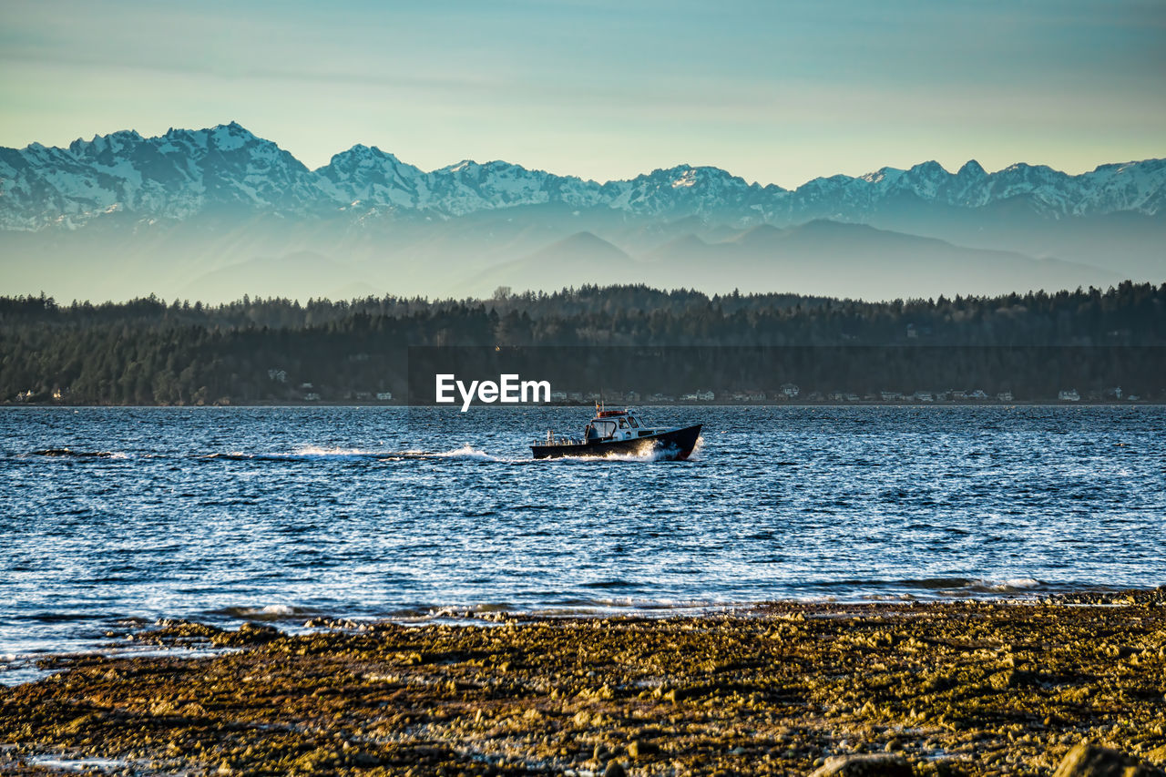 A boat cruises across the puget sound with the olympic mountains in the distance.
