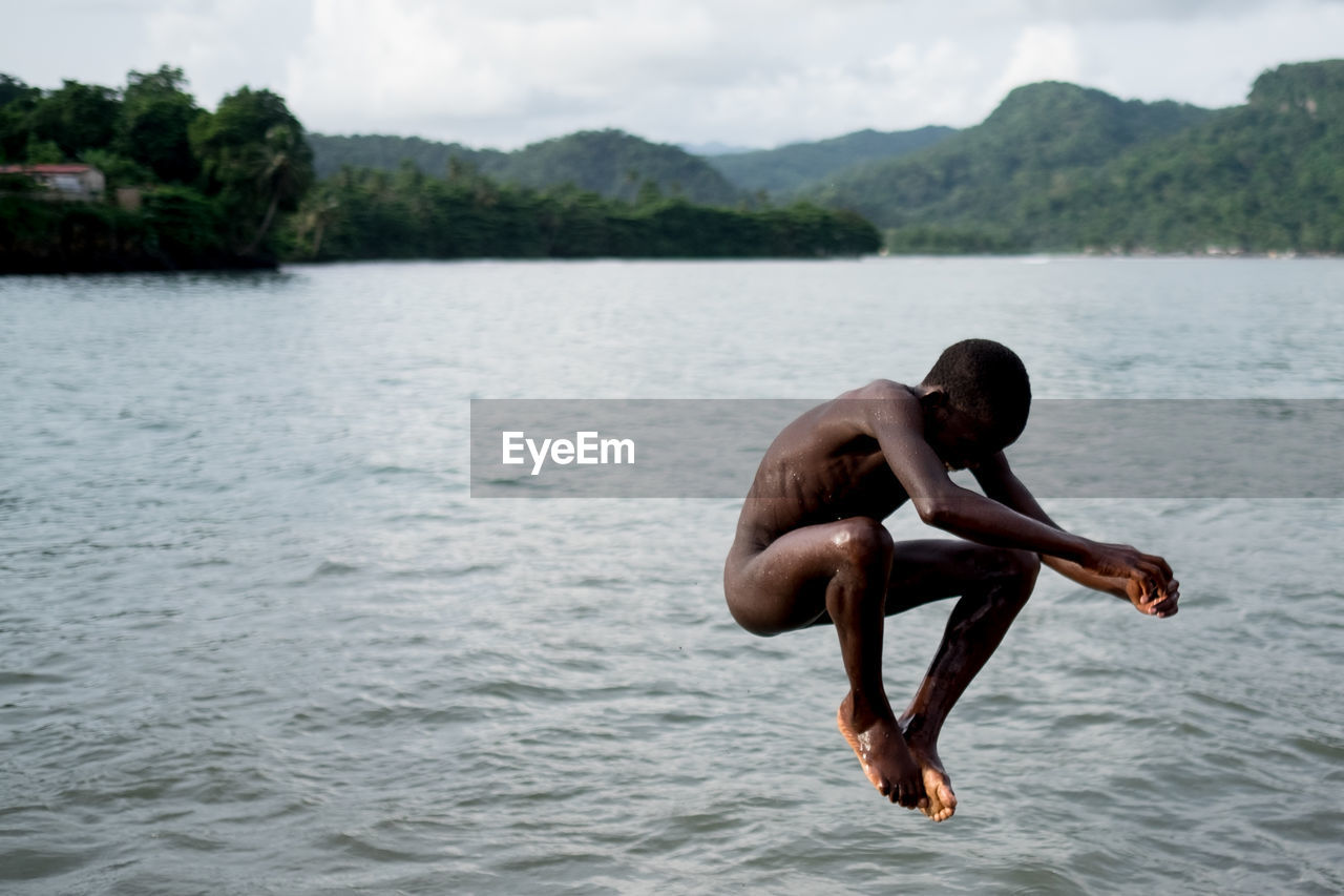 Full length of shirtless man in lake against sky