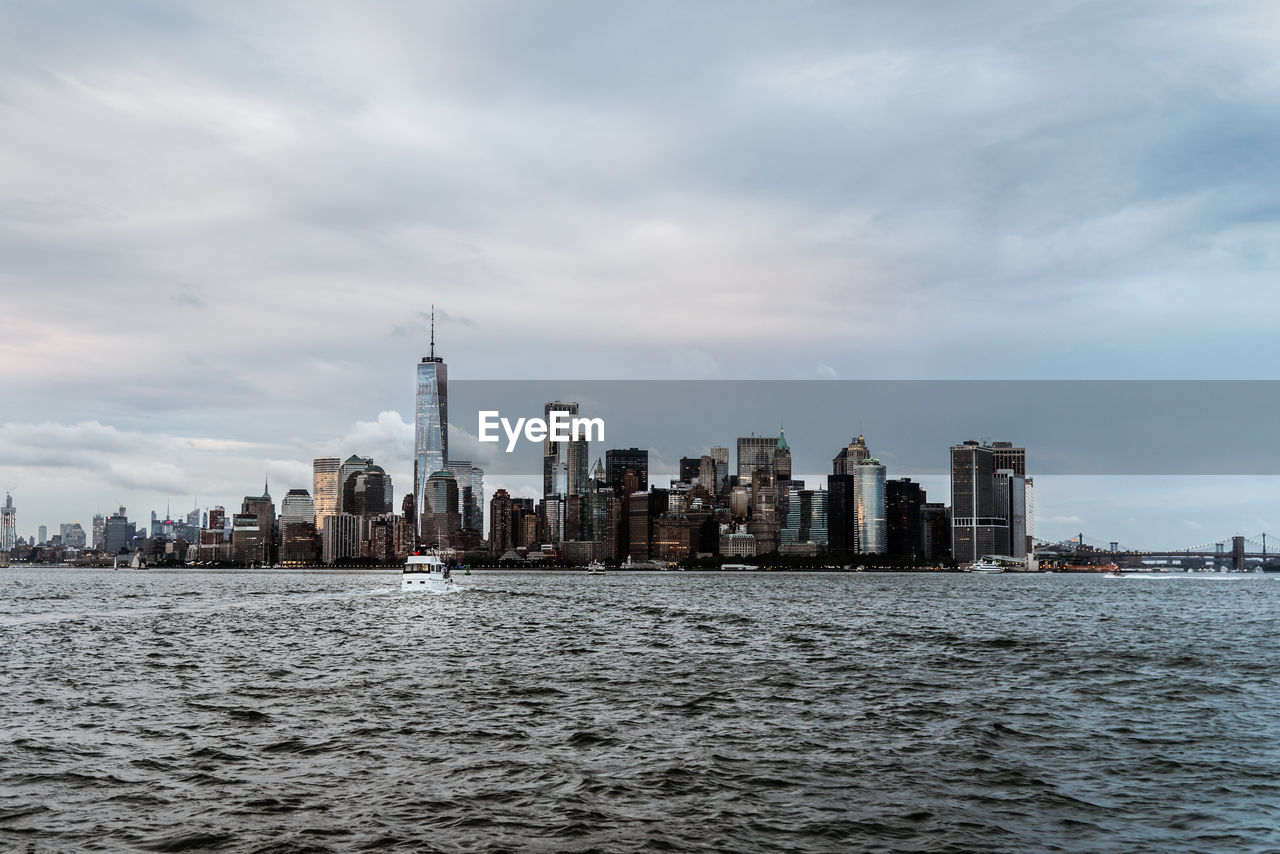 Sea by modern buildings in city against sky