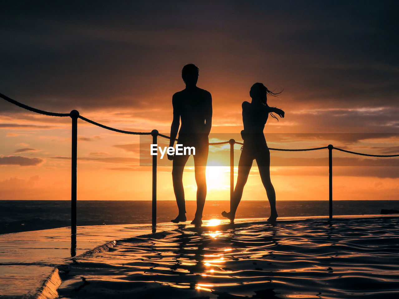 Silhouette people poolside by sea against sky during sunset