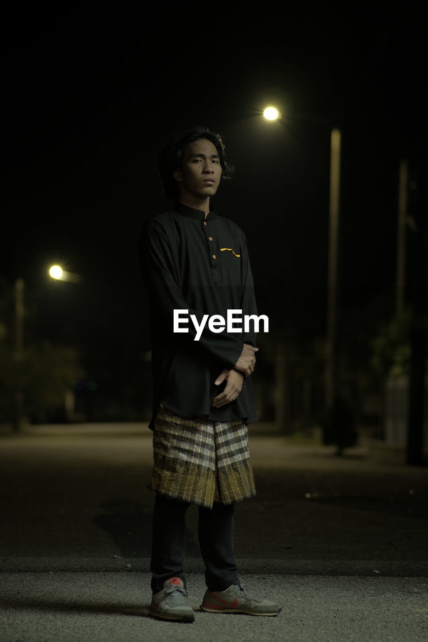 Young man looking away while standing on street at night