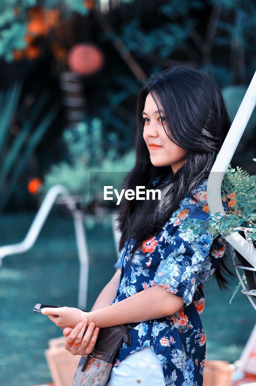 Side view of young woman using phone while leaning on railing