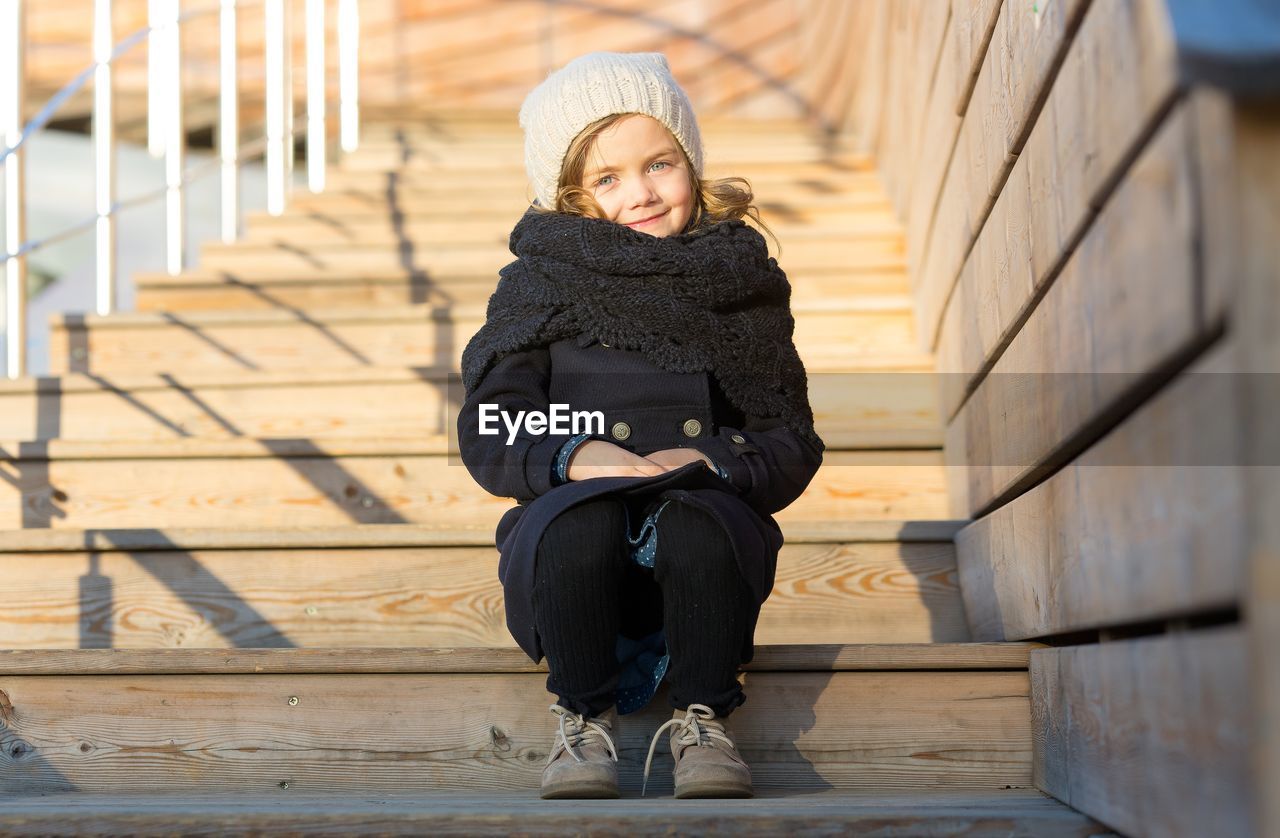 A five-year-old girl sits on wooden steps.