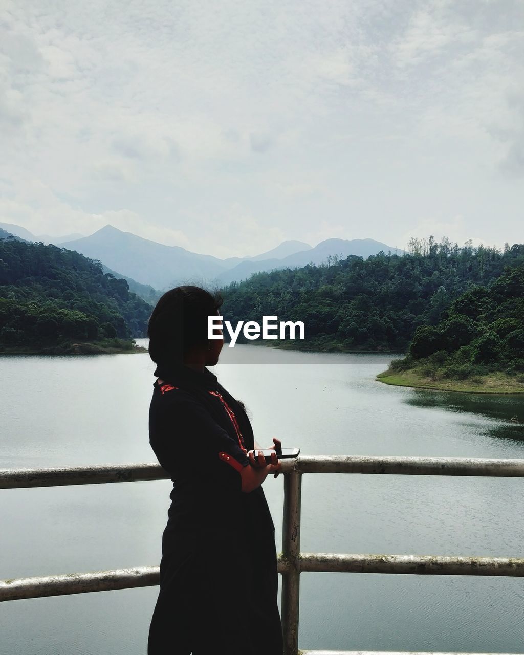 Side view of young woman standing on bridge over river against sky