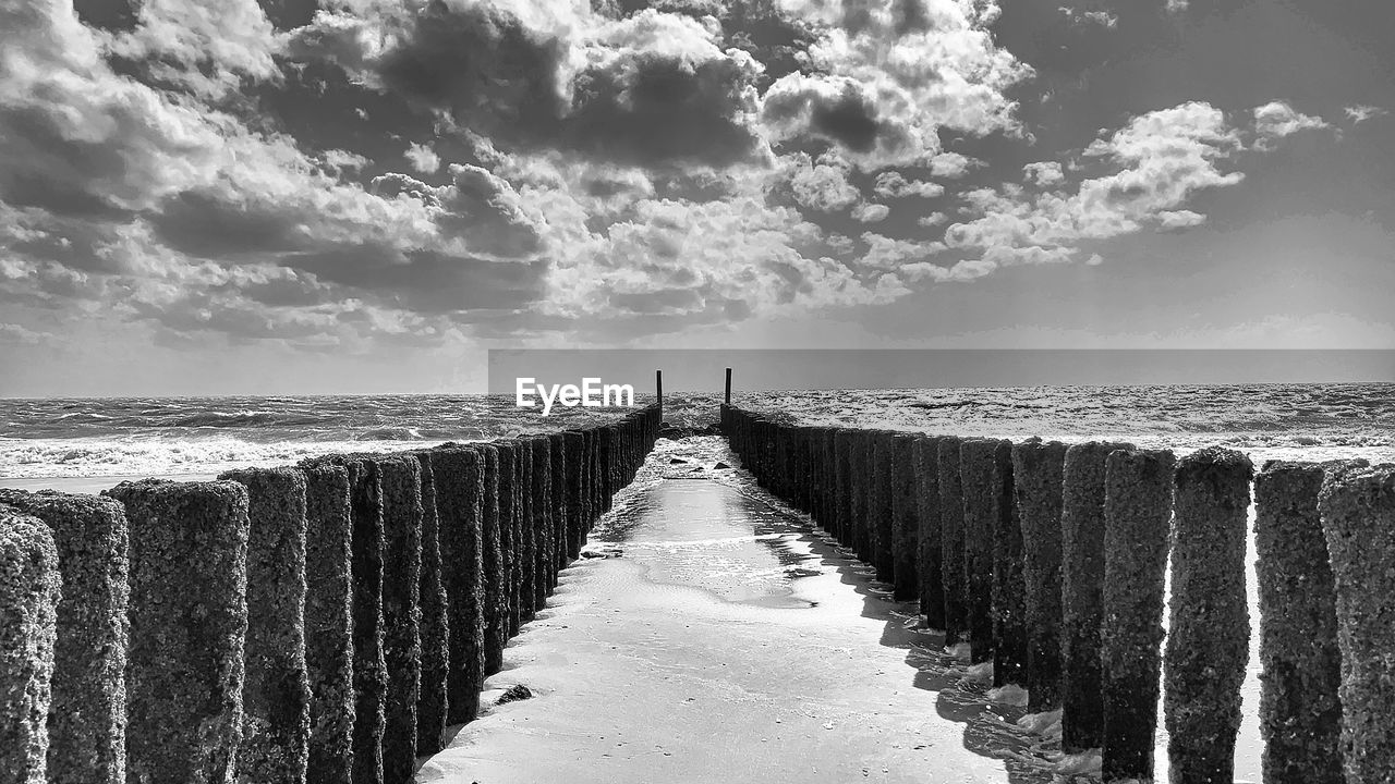 Wooden posts on footpath by sea against sky