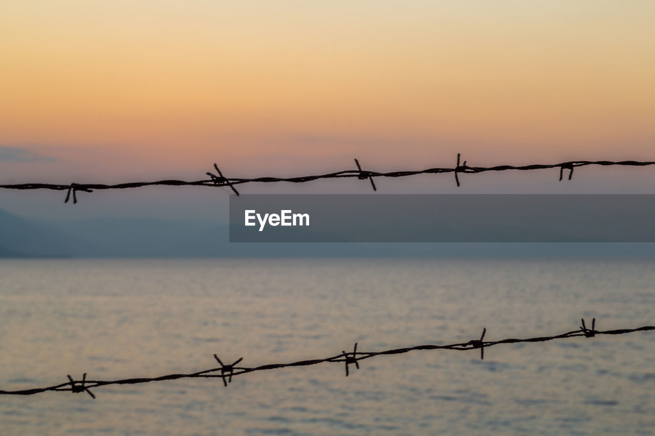 Close-up of barbed wire against sea during sunset