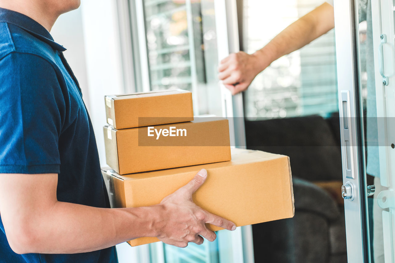 Midsection of man delivering packages to customer at door