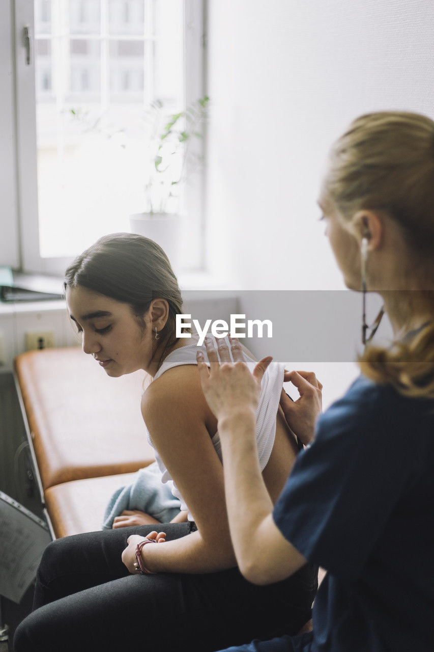 Female nurse examining girl using stethoscope in clinic