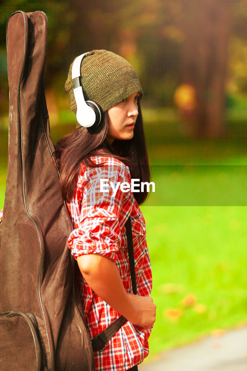 Woman with guitar listening music while standing on field