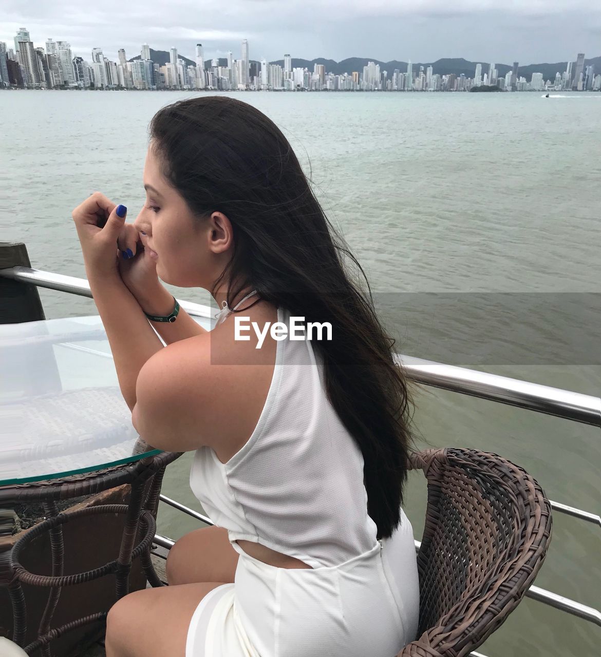 YOUNG WOMAN USING PHONE WHILE SITTING ON SEA