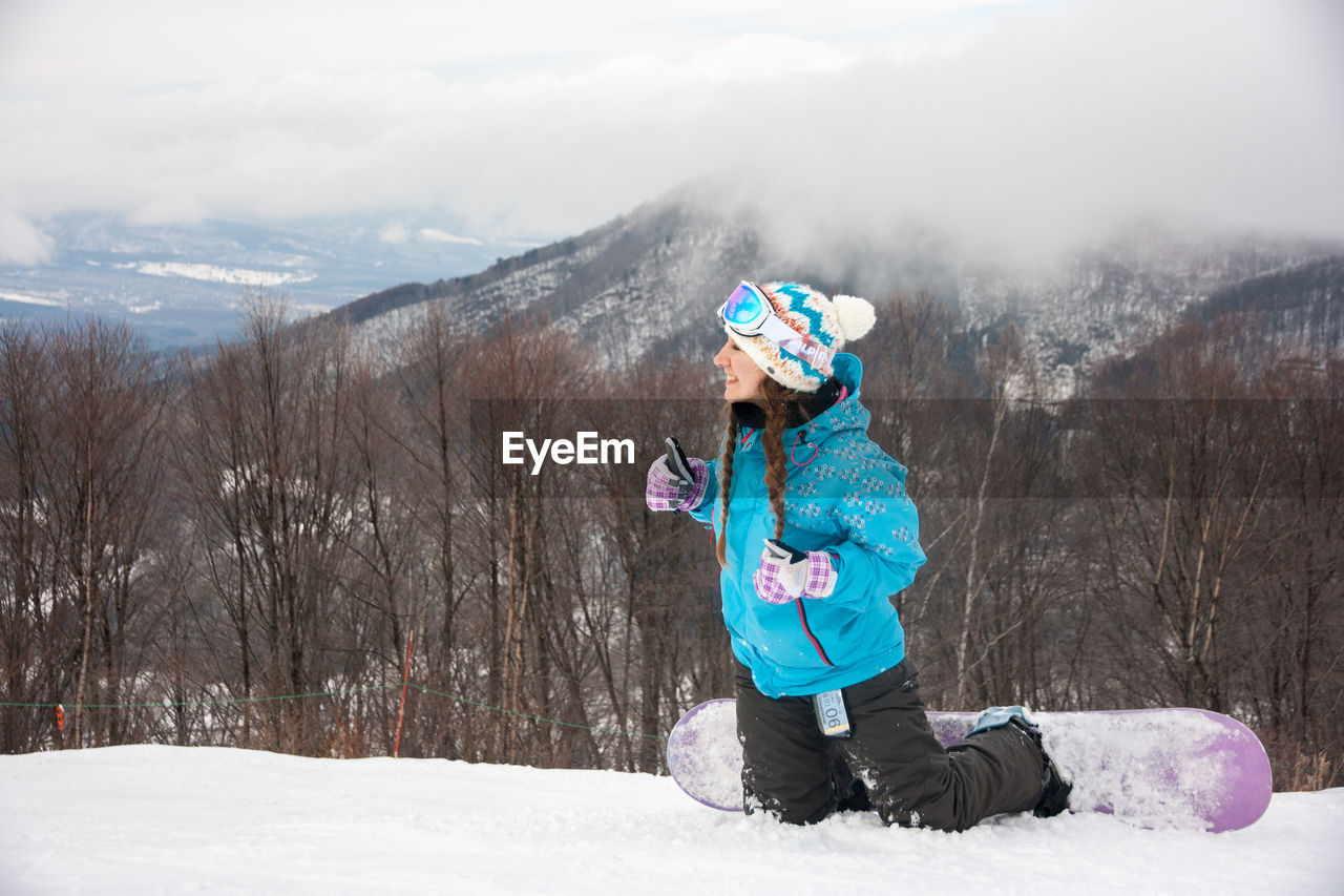 Woman snowboarding against bare trees