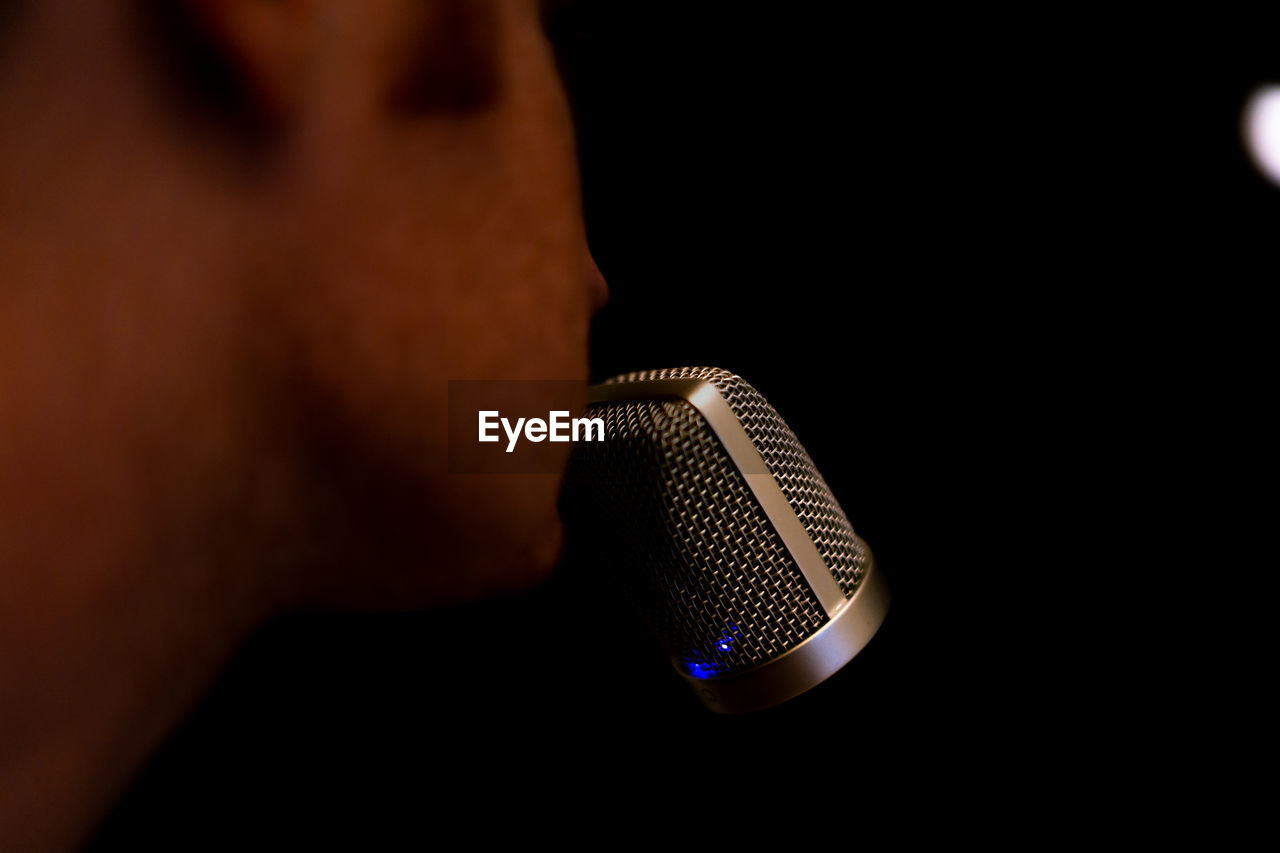 Cropped image of man singing on microphone against black background