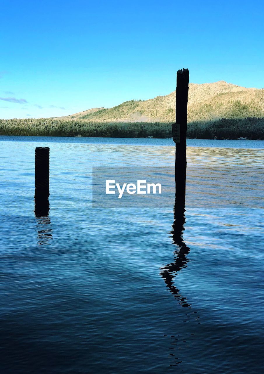 WOODEN POSTS IN LAKE AGAINST BLUE SKY