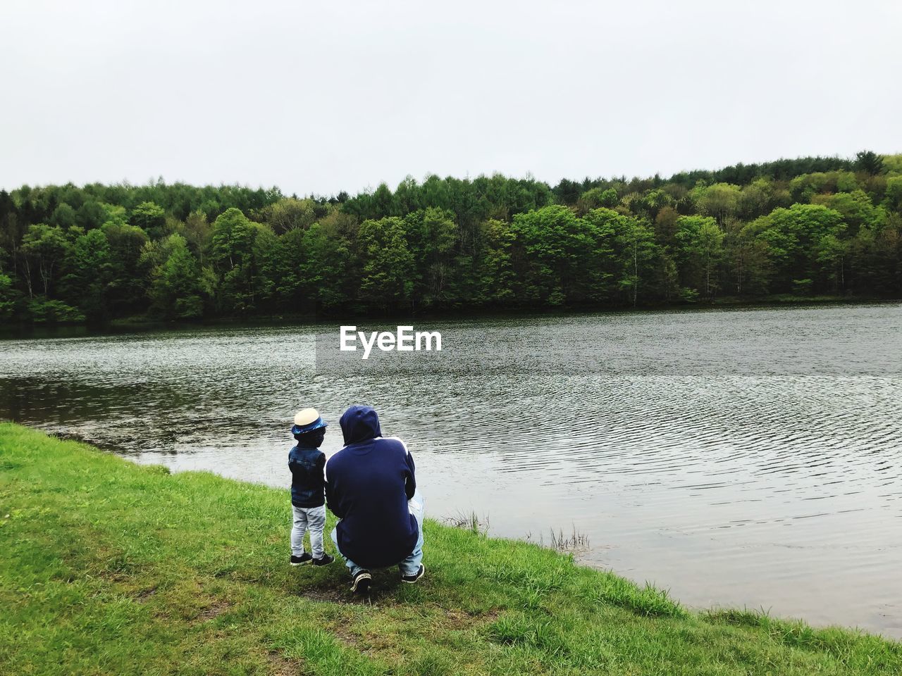 Rear view of father and child looking at lake against sky