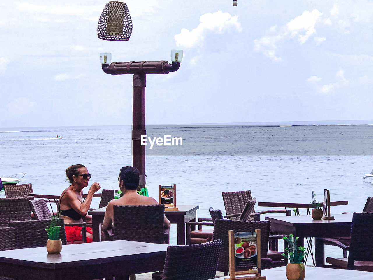 PEOPLE SITTING ON CHAIR AT BEACH AGAINST SKY