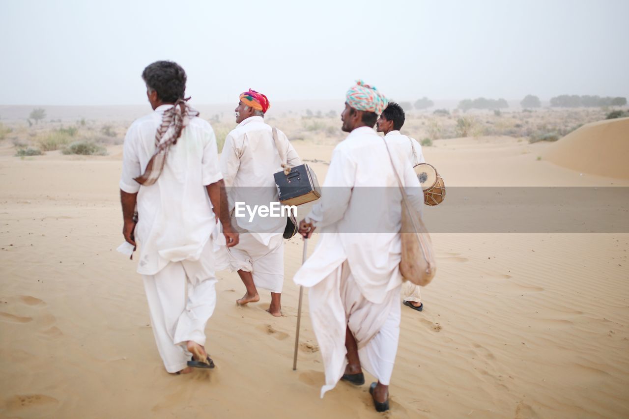 Rear view of people wearing traditional clothing walking at desert