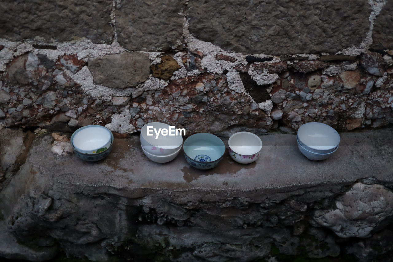 High angle view of empty bowls on seat against stone wall