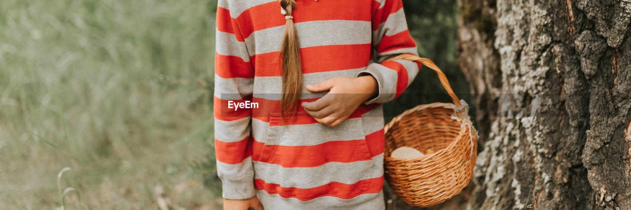 Kid girl mushroom picker is seek for and picking mushrooms with basket in the summer forest