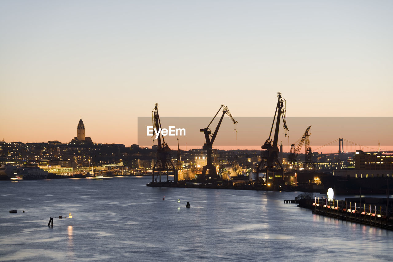 Silhouette cranes at commercial dock by gota canal against clear sky during sunset