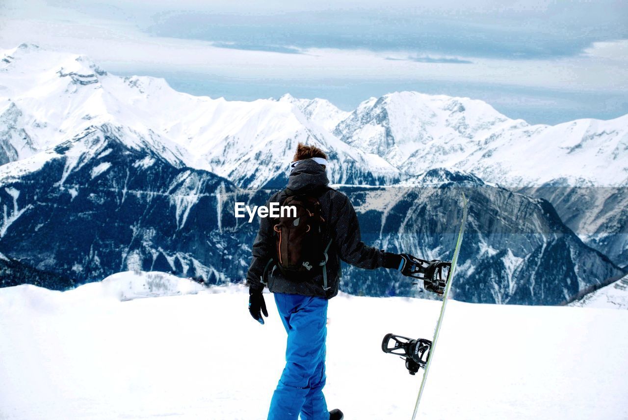 REAR VIEW OF WOMAN STANDING ON SNOW COVERED MOUNTAIN