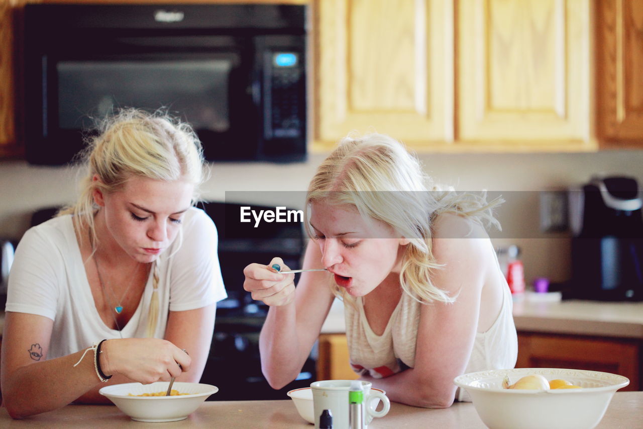 Sisters eating breakfast on table in kitchen
