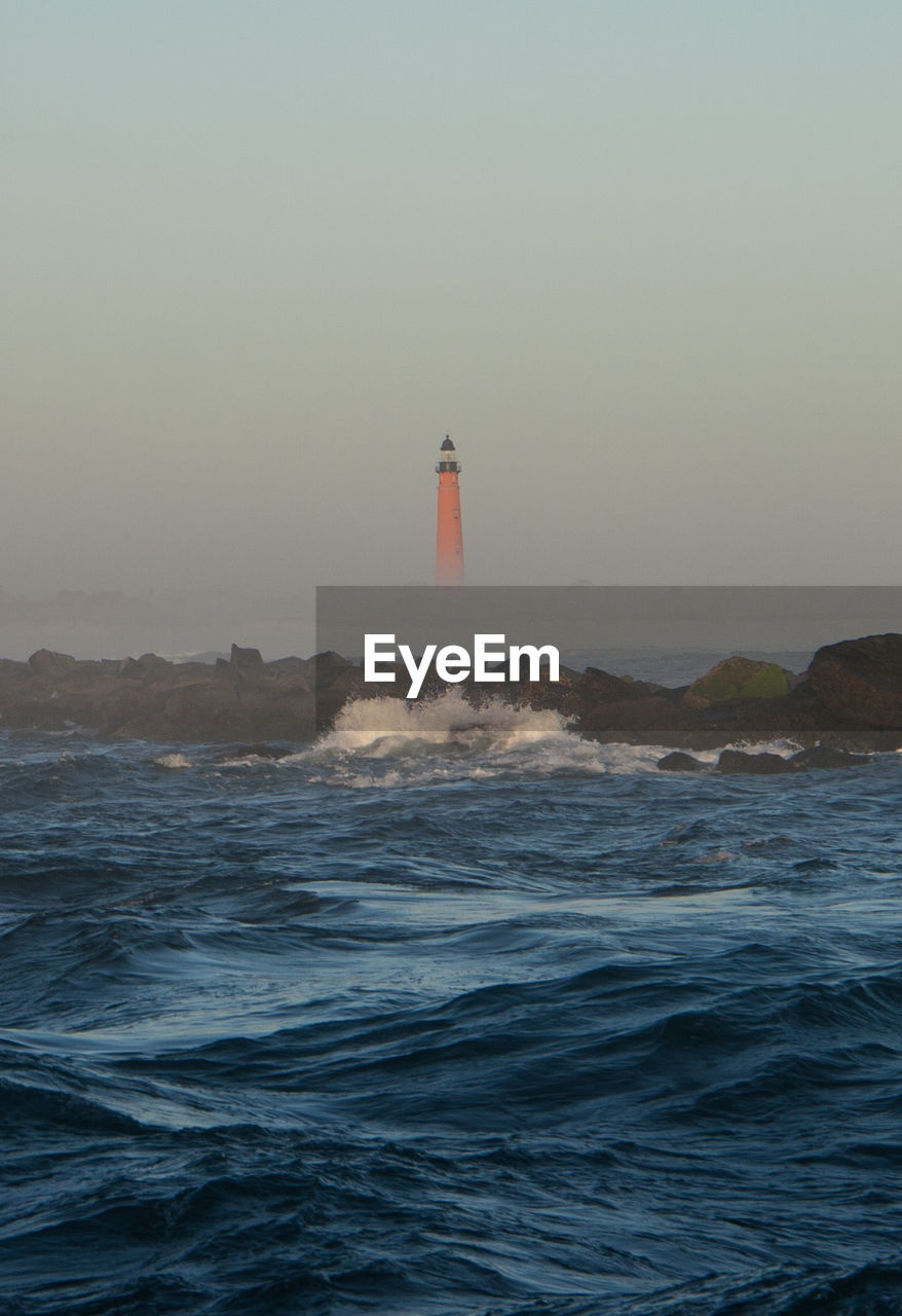 Lighthouse by sea against clear sky