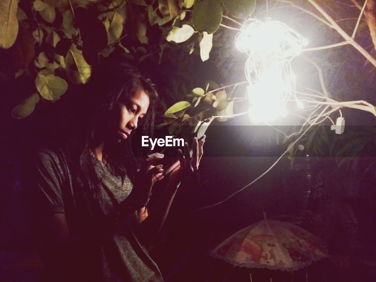 Young woman holding leaf by illuminated lights at night