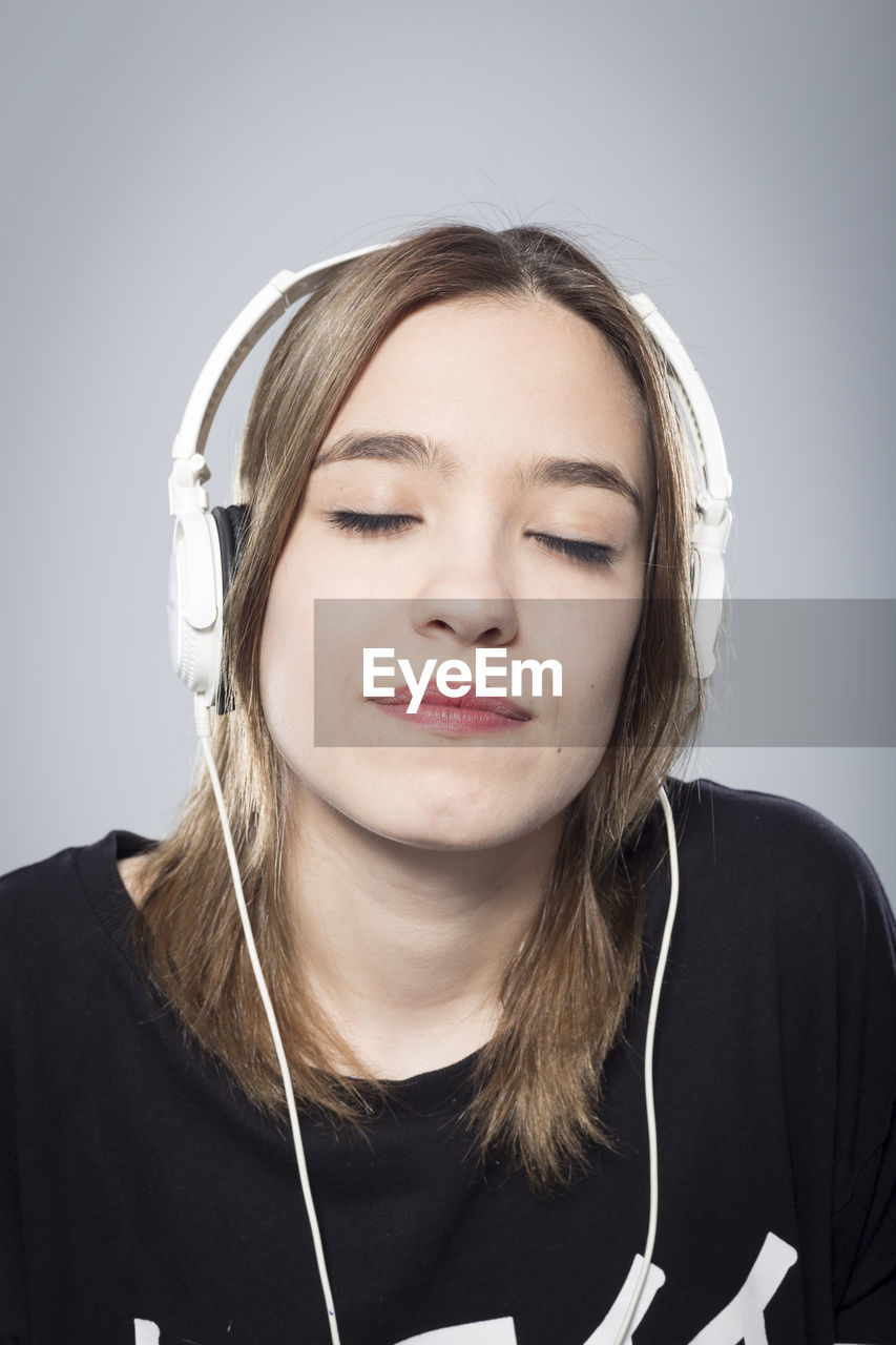 Close-up of young woman listening music against white background