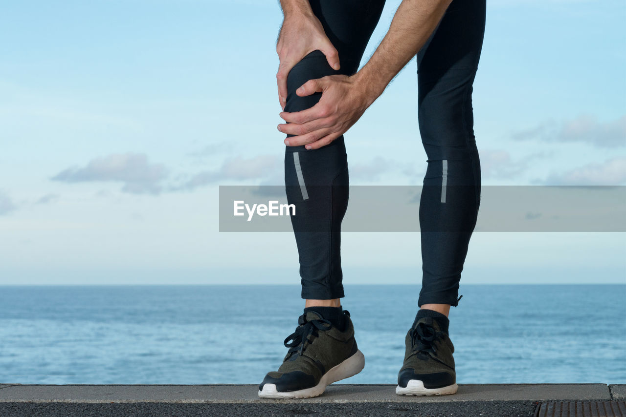 LOW SECTION OF MAN STANDING ON SEA AGAINST SKY