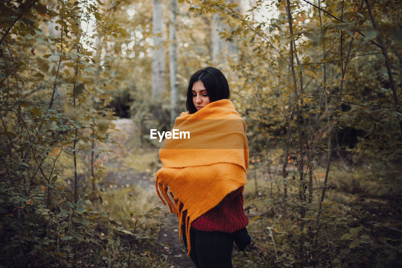 Woman dresses with her scarf inside the forest. autumn concept

